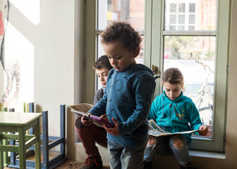 Drie kleine kinderen zijn aan het lezen in de speelruimte van Trafiek VZW.
