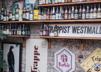 Een bakstenen muur vol met stoffige flesjes bier en reclame voor trappistbieren.