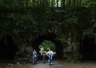Drie fietsers rijden onder de grot door. 