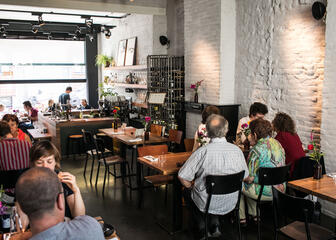 Eethuis met witte baksteenmuur, gasten aan bruine tafels, stoelen, open bar.