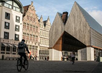 Een fietser voor de stadshal die gebouwd is uit hout, beton en glas en omringd wordt door oude gebouwen met getrapte daken. 