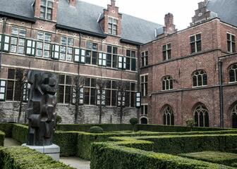 Zicht op middeleeuwse architectuur van het Pand, tuin met modern kunstwerk.