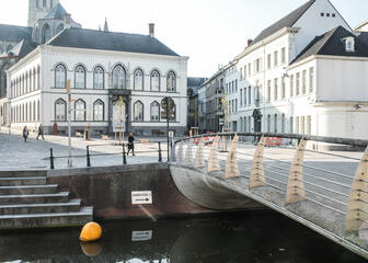 Open pleintje met groot wit Bisschopshuis, op de voorgrond brug en rivier.