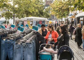 Marktkraam met jeans, drie vrouwen met kinderwagen bekijken de broeken.