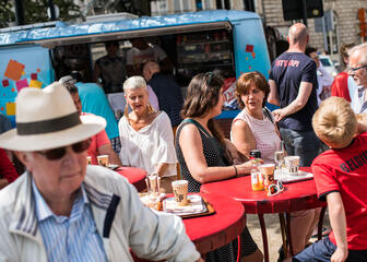 Mensen genieten van koffie aan hoge rode ronde tafeltjes bij de Foodtruck op de Kouter.