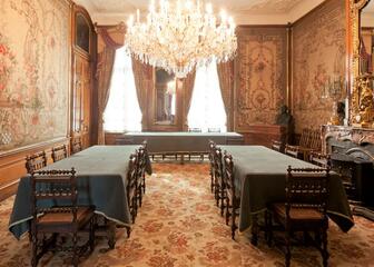 kamer met 3 tafels, stoelen, kroonluchter, casettehaard, behang en tapijt met bloemenpatroon