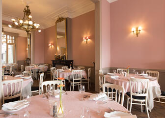 Gedekte ronde tafels in een chic interieur met roze muren en oude luchters. 