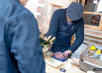 man die een oester opent, oesters op ijs in een houten krat, enkele champagneflessen, citroenen