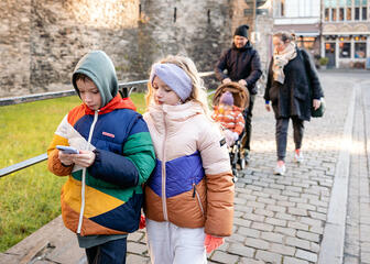 Twee kleurrijk geklede kinderen volgen de draakje Fosfor route op een smartphone