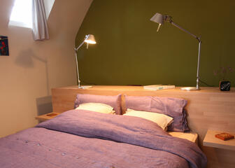 Tilia bedroom. The double bed is leaning against the large desk. Two desk lamps also serve as night lights.