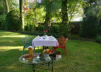 Ein gedeckter Frühstückstisch im Garten. Ein Tisch mit selbstgebackenem Brot, eine Obstschale und eine Schachtel mit Teebeuteln