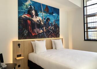 Room with double bed, wooden headboard and painting of Thorgal 