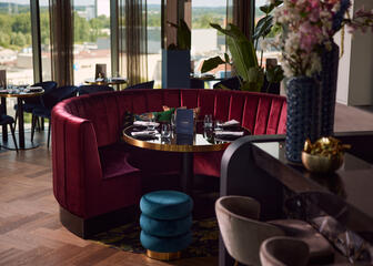 Imagen de un sillón redondo de color rojo oscuro, una mesa puesta y un puf azul oscuro. 