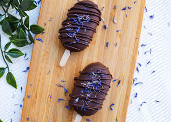 2 cakesicles enrobés de chocolat noir sur une planche en bois 