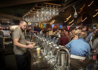 Barman taps beer while many visitors stand in the pub