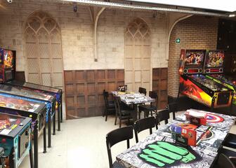 seating area with 4 pinball machines on the left side, tables in the middle and 2 pinball machines on the right side