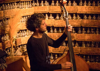 Man plays a double bass with wooden bins of beer bottles in the background