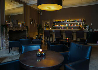 Lounge mit runden Tischen, schwarzen Ledersesseln und einer Bar im Hintergrund