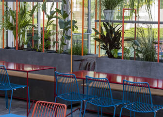 Terrasse avec chaises et tables en métal bleu et rouge et diverses plantes suspendues