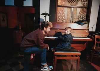 Enfant assis au piano avec un homme à côté de lui