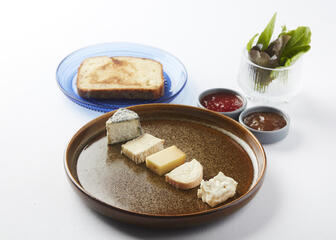 assiette brune avec fromages assortis, assiette bleue avec tranche de pain, 2 pots de chutney