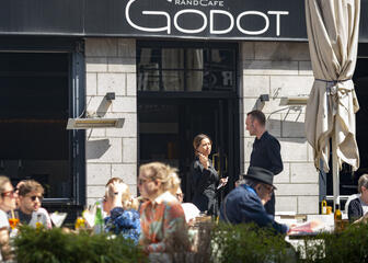Fachada de Godot, dos empleados conversan en un día soleado