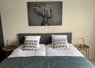 dubbel bed met witte lakens en groene bedsprei tegen een beige muur met schilderij