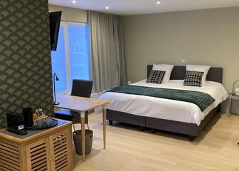 kamer met muren in groene tinten, dubbel bed met witte lakens en groene bedsprei