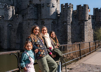 Tiany posiert mit ihren drei Töchtern an einem sonnigen Tag vor dem grauen Schloss der Grafen in Gent