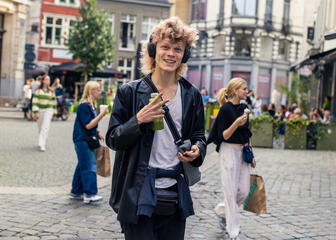 Der junge fröhliche Mann geht mit Kopfhörern durch die Straßen Gent