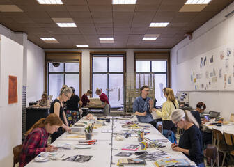 Een tiental kunstenaars werken samen aan een grote tafel.