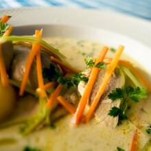 Une assiette de Gentse waterzooi : pommes de terre et poulet dans une assiette de soupe aux légumes. Vous voyez des carottes, du poireau et de l'oignon, le tout complété par du persil frisé.