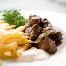 Een wit bord met Belgische frietjes en stoverij: rundsvlees in een bruine saus. Als salade zie je waterkers.
