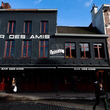 Zwarte voorgevel van Bar des Amis. Een toevallige passant staat op de foto en een dame die wacht voor de ingang.