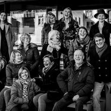 Groepsfoto met 15 lachende mensen, zwart-wit.