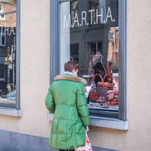 Vrouw met felgroene winterjas bekijkt etalage van Marthe. 