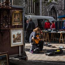 Gitarist op de Brocantemarkt bij Sint-Jacobs, kraam met schilderijen op de voorgrond.