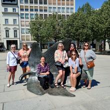 7 vrouwen poseren bij een metalen beeld van een boomblad