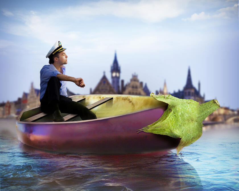 Ein Mann mit Schiffermütze sitzt in einem auberginefabenen Boot mit Graslei im Hintergrund