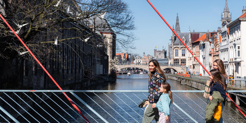 Tiany Kiriloff en haar drie dochters lopen over brug aan het water in Gent op zonnige dag