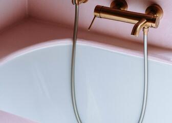 witte badkuip met vergulde mengkraan tussen roze muren 